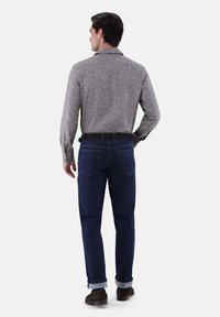 Herrenhemd in Grau mit Muster und langen Ärmeln, kombiniert mit dunkelblauen Jeans. Die Jeans sind an den Säumen hochgerollt, und ein schwarzer Gürtel wird getragen.