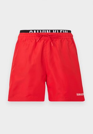 Piros férfi úszónadrág elasztikus derékpánttal, húzózsinórral, oldalzsebekkel és látható fekete Calvin Klein márkájú belső derékpánttal.