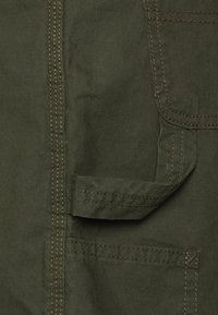 Olijfgroene stof met een gladde textuur, voorzien van een utility-pocket, zichtbare stiksels en een schoon ontwerp zonder versieringen.