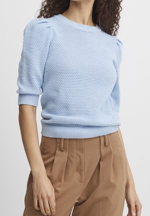 Lys blå, tekstureret striktrøje med puffede ærmer og ribbede manchetter. Stylet med højttaljede beige bukser.