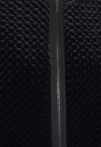 Black zip-up jacket featuring a textured, plush fabric with a geometric pattern. The zipper is metallic and centrally placed.