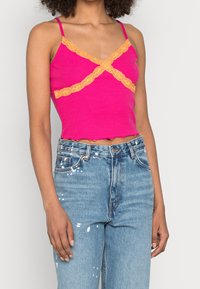 Tight rosa linne med orange spetsdetalj och vågig fåll. Matchas med hög midja jeans i ljust tvättad, slitna blå.