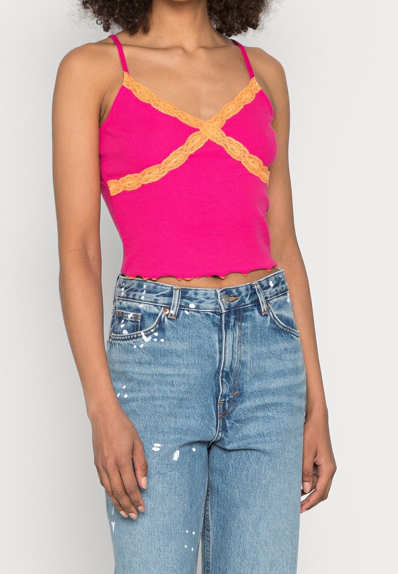 Tight rosa linne med orange spetsdetalj och vågig fåll. Matchas med hög midja jeans i ljust tvättad, slitna blå.