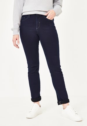 Dunkelblaue Jeans mit slim fit, ausgestattet mit fünf Taschen, dezentem Steppund leicht hochgerollten Säumen, kombiniert mit weißen Sneakers.