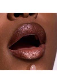 Lähelle huulia, joissa näkyy rikas metallinen ruskea sävy hohtavalla pinnalla. Tekstuuri näyttää sileältä ja kiiltävältä, korostaen huulien täyteläisyyttä.