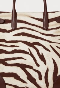 Canvas draagtas met een bruin en crème zebra-strijkpatroon, voorzien van bruine leren handvatten en accenten. De gestructureerde oppervlakte voegt visueel interesse toe.