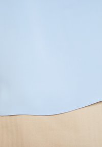 Blouse bleu clair avec une texture lisse, ourlet arrondi et sans motifs visibles, superposée à un tissu beige texturé avec un motif chevron.