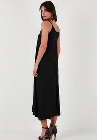 Schwarzes, ärmelloses Maxikleid mit relaxed Fit, ausgestattet mit einem Rundrücken und Seitenschlitzen. Aus weichem, leichtem Stoff gefertigt.