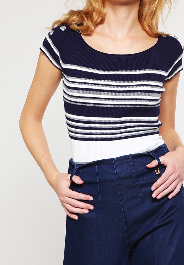 Marinblå randig stickad topp med vita accenter och korta ärmar. Har knapppdetaljer på axlarna. I kombination med högmidjade marinblå byxor.