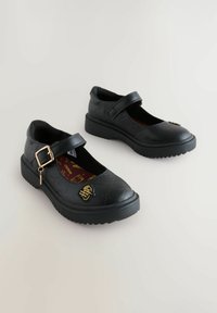 Des chaussures Mary Jane noires avec une finition texturée, dotées d'une sangle avec une boucle dorée et d'une semelle intérieure à motifs. Semelle en caoutchouc légèrement surélevée.