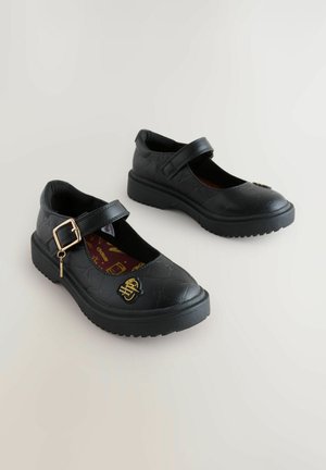 Des chaussures Mary Jane noires avec une finition texturée, dotées d'une sangle avec une boucle dorée et d'une semelle intérieure à motifs. Semelle en caoutchouc légèrement surélevée.