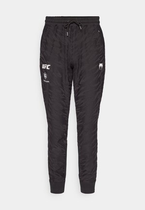 Černé joggingové kalhoty s texturovaným vzorem, elastickým páskem se šňůrkou a logo akcenty na přední straně. Manžety na kotnících.