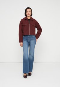 Κοντό μπορντό σακάκι με φερμουάρ και δύο τσέπες στο στήθος, συνδυασμένο με φαρδιά μπλε τζιν. Το μοντέλο φοράει σκούρα παπούτσια, σε φόντο απλό.