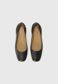 Ballerines en cuir noir avec des bouts carrés, texture lisse, bords élastiqués et un subtil accent doré près du talon. Semelles intérieures beiges visibles.