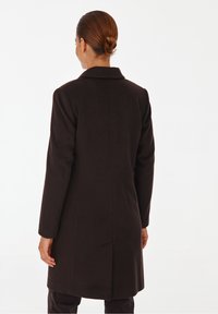 Manteau en laine marron foncé avec un col cranté, des manches longues et une coupe ajustée, présentant une fente simple à l'arrière pour faciliter les mouvements.
