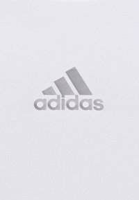 Weißes Sportshirt mit einem grauen Adidas-Logo und drei Streifen. Glatte Textur mit passgenauer Form. Keine zusätzlichen Muster oder Akzente.
