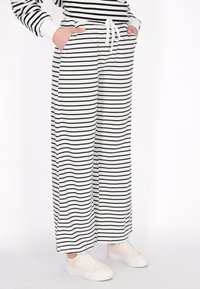 Pantaloni a gamba larga a righe bianche e nere con vita elastica e cordino, dotati di tasche laterali e un morbido tessuto.