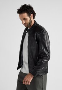 Zwart leren jack met een gladde textuur, ritssluiting en een staande kraag. Bevat subtiele schouderaccenten en zijzakken met rits.