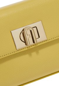 Geel gestructureerde leren clutch met een glanzende gouden sluiting met een logo. Gladde afwerking en contrasterende stiksel details langs de randen.