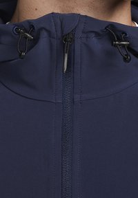 Gros plan d'une fermeture éclair d'une veste bleu marine entièrement zippée, avec des cordons de serrage réglables de chaque côté du col montant.