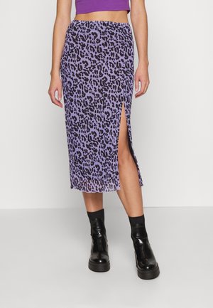 Kvinde iført et lilla midinederdel med leopardprint og en frontslids ved låret, sorte ankelstøvler og en lilla cropped top mod en ensfarvet baggrund.