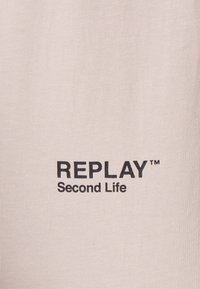Tela de algodón beige con el logo "REPLAY" en letras negras negritas, y "Second Life" en texto más pequeño debajo. Textura suave y diseño simple.