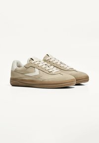 Beige sneakers med overdel i ruskind, kontrasterende teksturerede detaljer, cremefarvede snørebånd og sål i gummi. Low-top design med syninger.