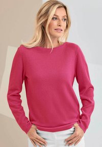 Roze gebreide trui met lange mouwen, ronde hals en ribgebreide onderrand. Zachte textuur met een gladde afwerking, gedragen met lichtgekleurde broeken.