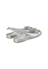 Sandali piatti metallici argento con cinturini alla caviglia regolabili, impreziositi da accenti circolari davanti e una suola testurizzata.