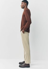 Brauner Strickpullover, beige Hose und dunkelbraune Slipper. Die Silhouette ist lässig und angepasst, mit einer glatten Textur und dezentem Design.