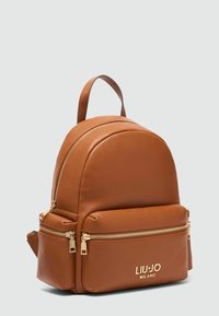 Sac à dos en cuir brun avec un design arrondi, deux compartiments zippés, des accents en matériel doré et un logo bien en évidence à l'avant.