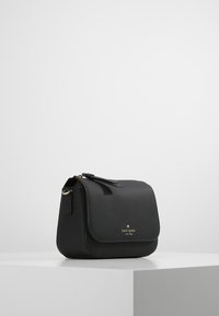 Černá kožená taška přes rameno s texturovaným povrchem, zlatými doplňky, klopou na zavírání a logem umístěným vepředu.