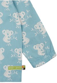 Tessuto azzurro chiaro a maniche lunghe con motivo di koala bianco e etichetta verde "loud + proud". Texture morbida con polsini elastici.