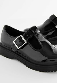 Zwarte gepatineerde leren schoenen met een T-strap en zilveren gespdetails. De zool is dik en getextureerd voor grip. Heeft een ronde neus design.