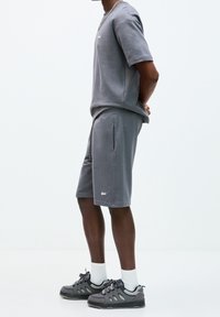 Ensemble t-shirt et short en coton gris avec une coupe décontractée. Le t-shirt affiche un logo, et le short possède des poches latérales. Porté avec des chaussures de sport grises.