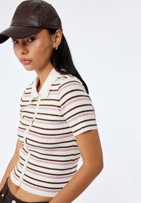 Top de punto acanalado a rayas en blanco, rosa claro y marrón. Mangas cortas, diseño con cuello y cierre de botones con un ajuste ceñido.