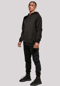 Black hooded sweatshirt with a kangaroo pocket, paired with tapered black cargo pants and black high-top sneakers. Smooth texture, casual design.