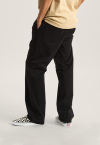 Sorte, løstsiddende bukser med sidelommer, kombineret med sort-hvide ternede slip-on sko. Glat stof og lige ben design.