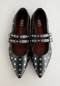Ballerine in pelle nera con punta affusolata, decorate con borchie argento e doppie cinghie con fibbie metalliche. Interno marrone.