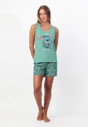 Mujer con camiseta sin mangas verde con dibujo animado de Stitch y texto "Not Today Vacation Mode", combinada con pantalones cortos verdes con estampado tropical.