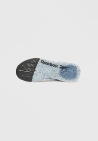 Pohja Reebok-kengästä, jossa on musta ja pilkullinen vaaleansininen kumipohja, tekstuuriset pito-kuviot ja Reebok-logo kaaren lähellä.