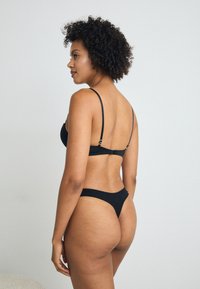 Black lingerie set featuring a bralette with thin straps and a bikini bottom. Soft fabric with minimal coverage and a sleek design.