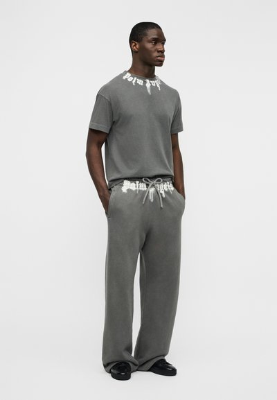 Γκρι βαμβακερή μπλούζα με το γραφικό "Palm Angels" στο λαιμό, συνδυασμένη με αντίστοιχο παντελόνι φόρμας με κορδόνι στη μέση και τσέπες.