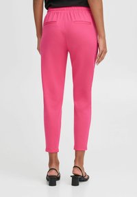 Rosa, dehnbare Hose mit elastischem Bund, schmal zulaufendem Schnitt und zwei Gesäßtaschen, kombiniert mit schwarzen Absatzsandalen.