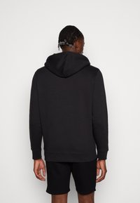 Zwarte hoodie van zacht materiaal, met een grote capuchon, lange mouwen, geribde manchetten en een relaxte pasvorm, gecombineerd met zwarte shorts.