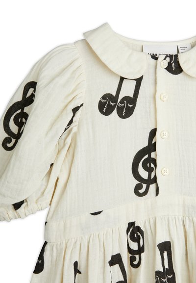 White dress with black musical note patterns, featuring a rounded collar, button closure, and gathered puff sleeves in textured fabric.