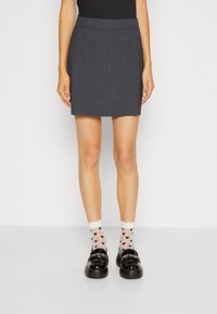 Jupe mini gris foncé à coupe droite et fente latérale. Portée avec des mocassins noirs brillants et des chaussettes blanches ornées de petits cœurs bleu marine.