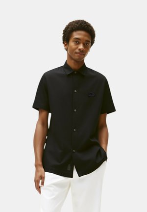 Camicia nera a maniche corte con bottoni, dal colletto ben definito, caratterizzata da un discreto logo ricamato sul petto e una superficie in tessuto liscia.