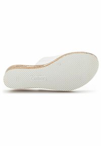 Chaussures plates blanches avec une semelle en caoutchouc texturé. Présente un talon incurvé et un logo au bas. Le matériau semble lisse avec un minimum de détails.