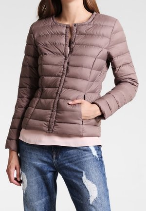 Giacca puffer trapuntata marrone con scollo rotondo, bottoni frontali e tasche laterali, sovrapposta a una maglia rosa pallido, abbinata a jeans strappati.
